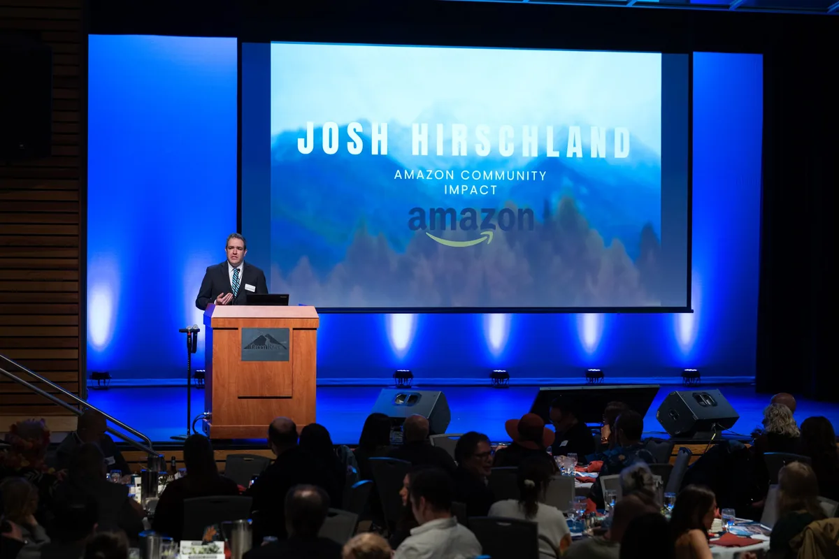 Josh delivering the keynote at the Covington Storehouse Gala, his name on the screen behind him and the room seated in front